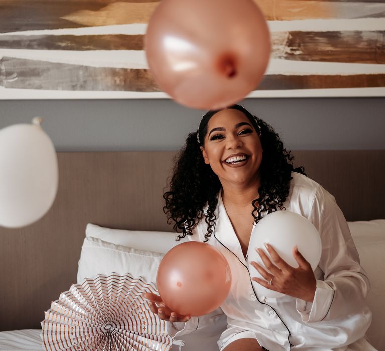 Black bride laughs in front of rose gold balloons on the morning of her wedding day