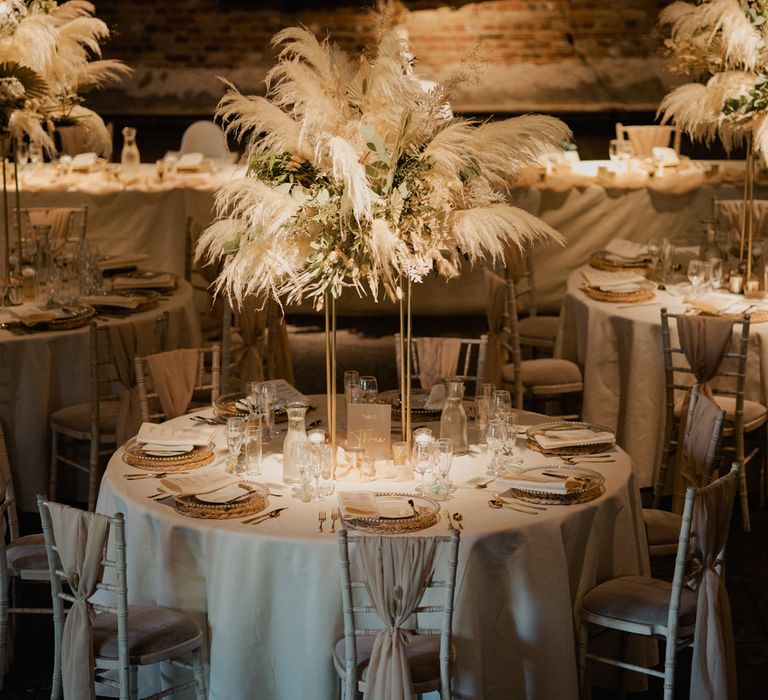 Round tables at Cooling Castle Barn wedding reception with tall pampas grass centrepiece decor 