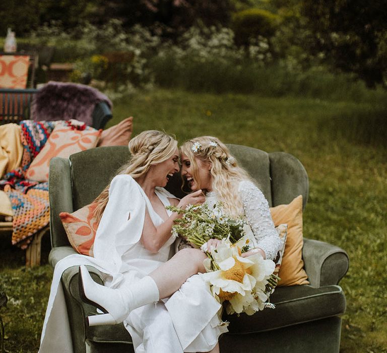 Two brides sitting on a retro sofa at their outdoor sixties wedding 