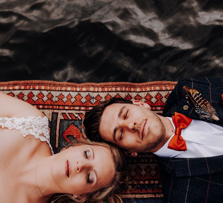 Bride & groom lie together side by side on the jetty with one another 