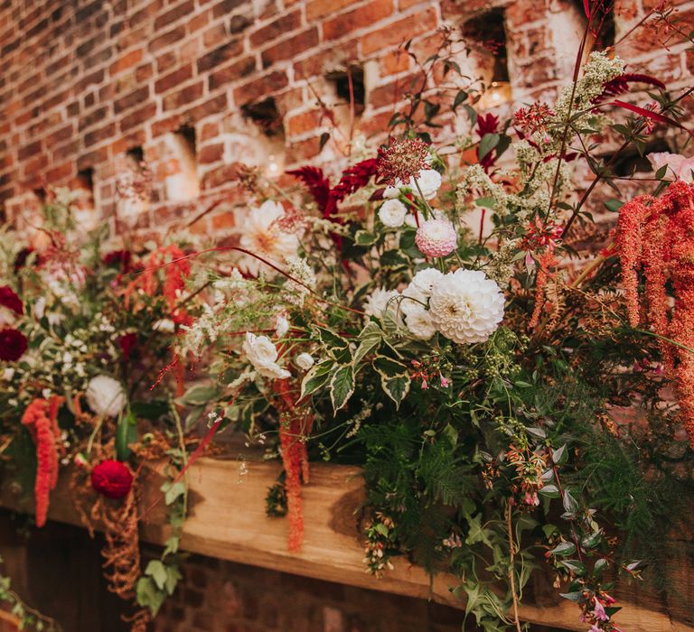 Red, green and white flowers over large fireplace in red brick barn for rustic wedding