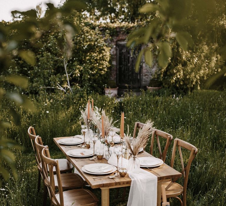 Outdoor tablescape in a meadow with wooden table and chairs, dried flowers and round wedding welcome sign