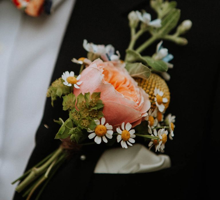 Groom in a black suit and floral tie with a coral rose buttonhole flower 