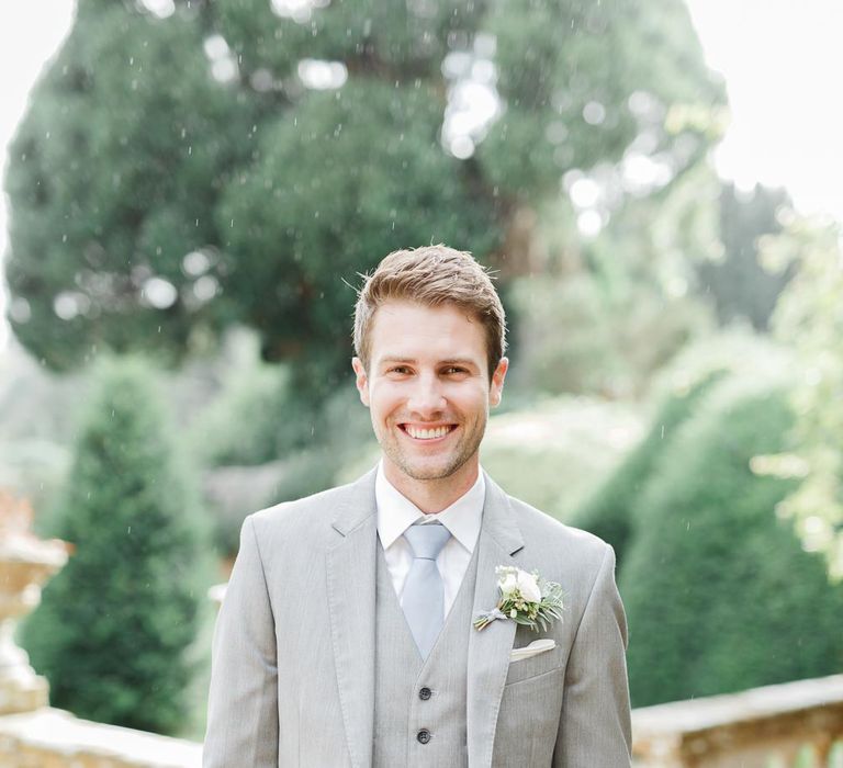 Groom in a pale grey three-piece wedding suit with blue tie and white buttonhole flower