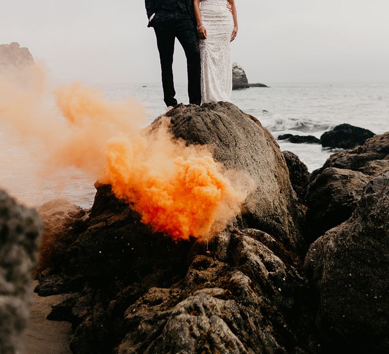 Coastal couples wedding photography with an orange smoke bomb let off on a cliff 