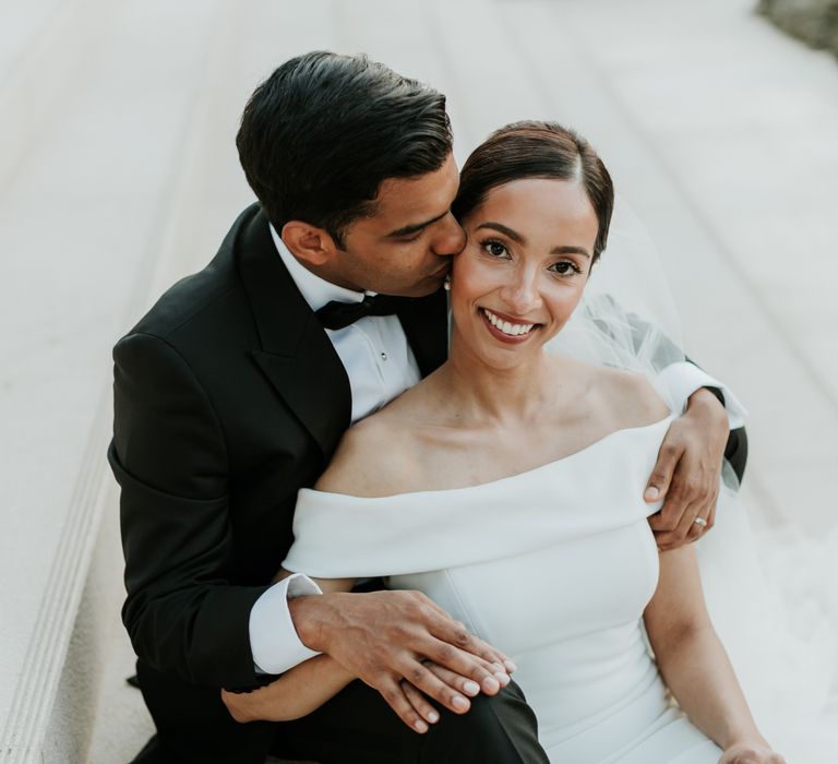 Grooms kisses his brides cheek as they sit on steps on their wedding day | Hannah MacGregor Photo & Film