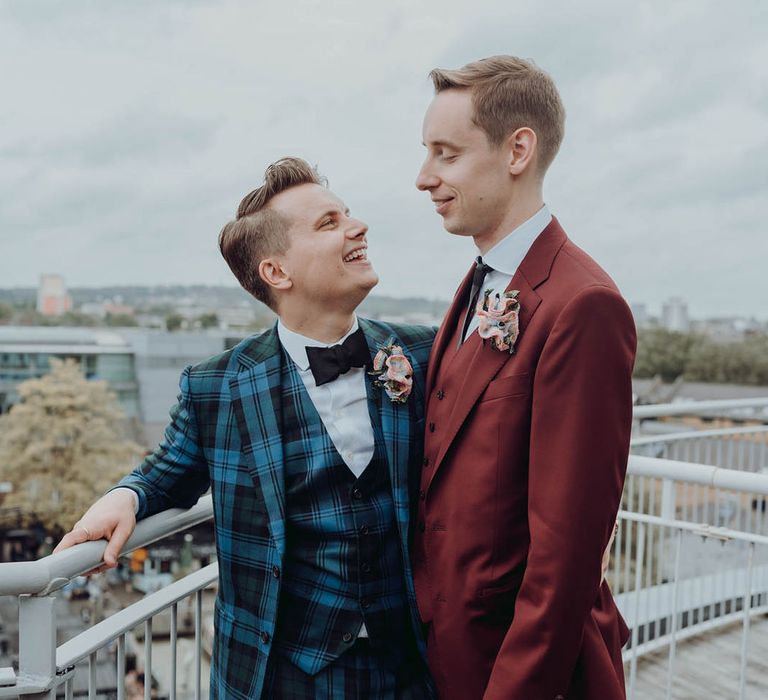 Grooms stand on balcony as they look lovingly at one another after cinema wedding | Kim Williams Weddings