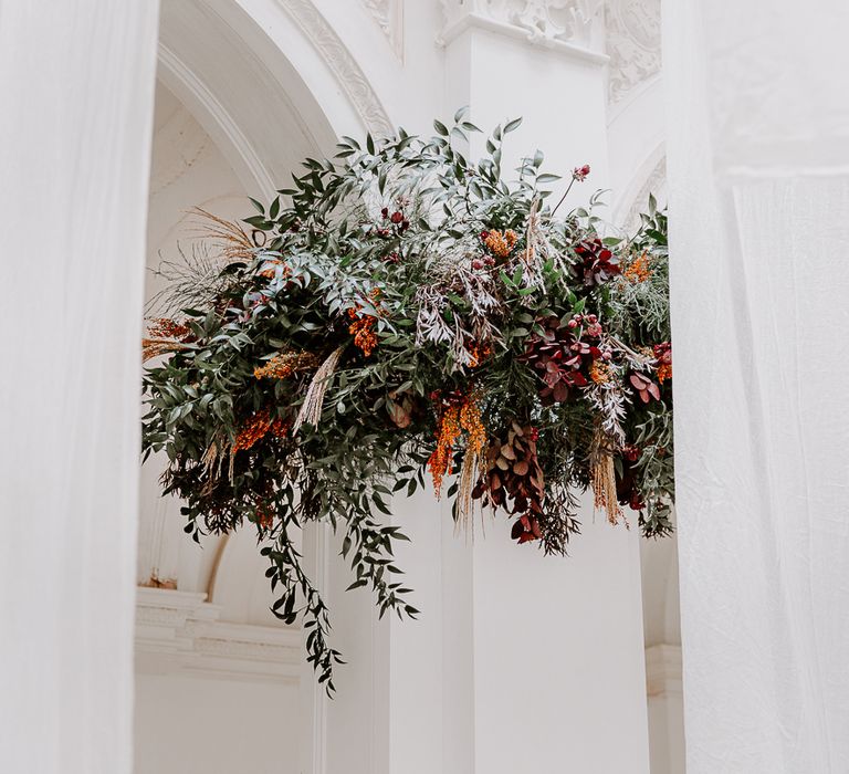 Floral arrangements around the pillars at Bylaugh Hall with foliage, orange and red flowers 