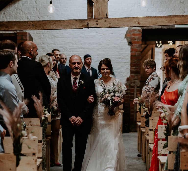 Bride in an embellished wedding dress walking down the aisle at Woolas Barn with her father 