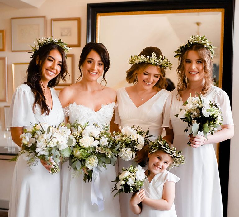 Bridesmaids stand with bride and flower girl as they wear white dresses and wear floral crowns 