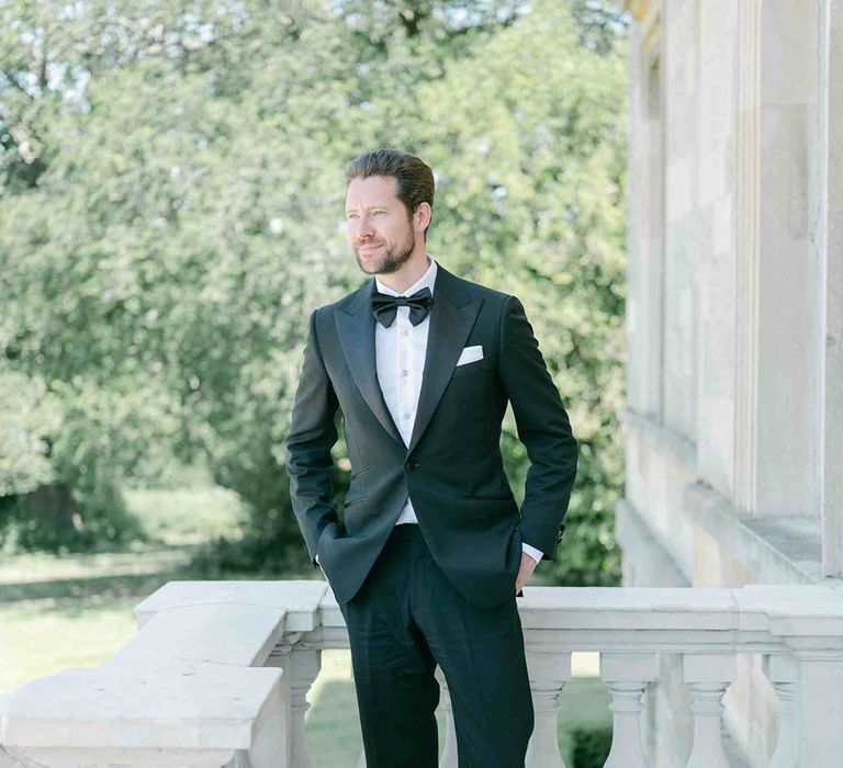 Groom in a black suit with bow tie standing on a balcony at Botley's Mansion in Surrey 