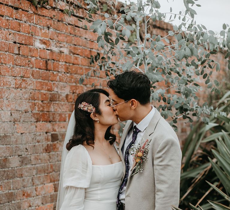 Bride & groom kiss as bride holds colourful floral homemade bouquet