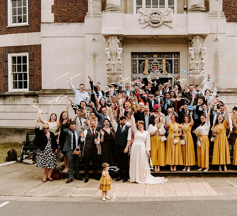 Wedding party stand on staircase whilst holding streamers in the air after ceremony