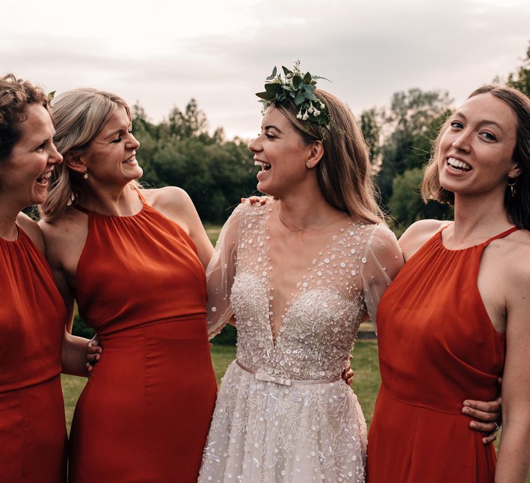 Bride in v neck long sleeve Julie Vino wedding dress and boho flower crown laughs with bridesmaids in red halter neck bridesmaid dresses 