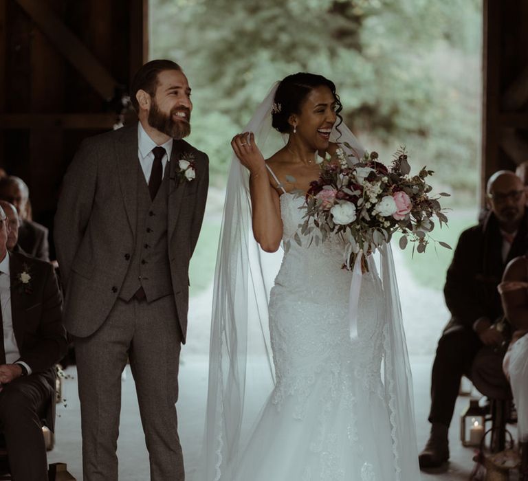 Bride walks down the aisle whilst carrying floral bouquet at Nancarrow Farm