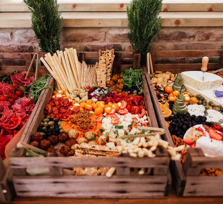 Multicoloured grazing boxes in wooden crates with cheeses, charcuterie and crackers for festival style wedding