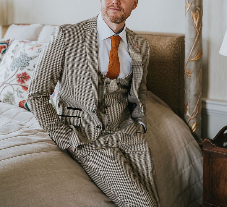 Groom in a three-piece beige dogtooth wedding suit with horseshoe waistcoat ad orange waffle tie 