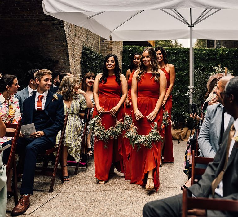 Bridal party in burnt orange bridesmaid dresses walking down the aisle holding foliage hoop bouquets at 100 Barrington wedding 