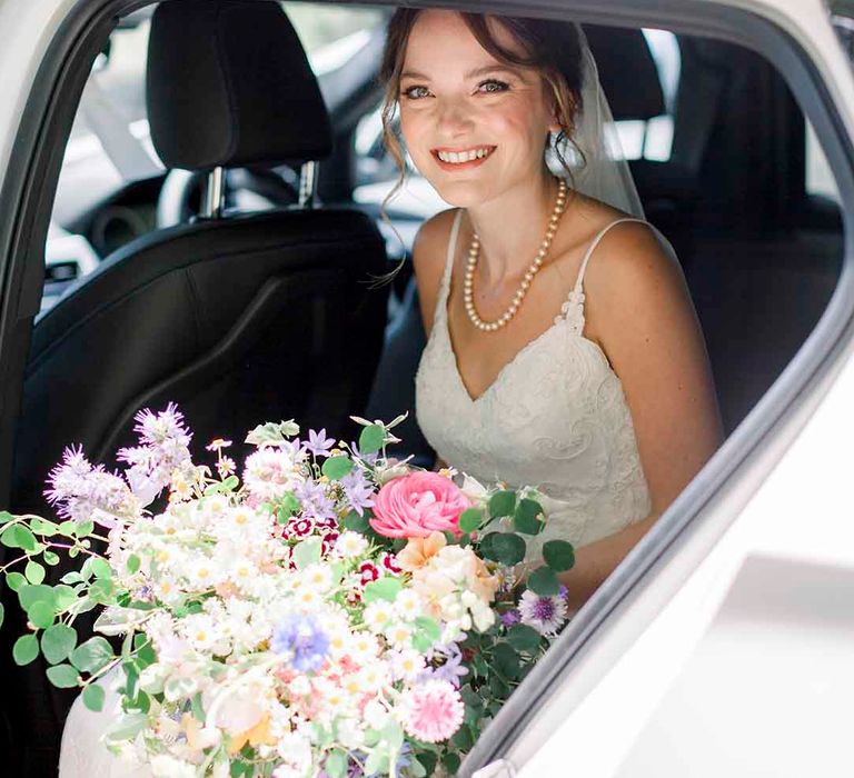 Bride sits in car and holds pastel bouquet 