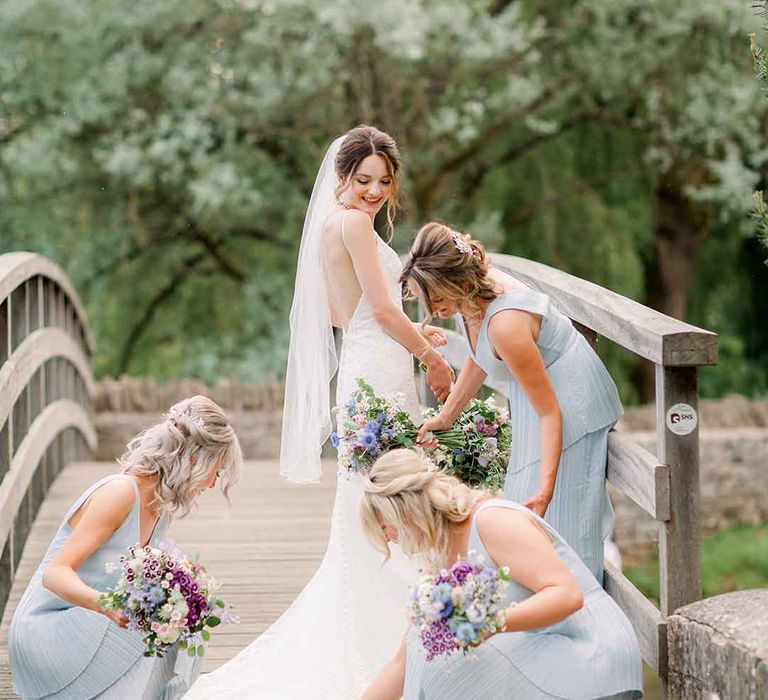 Bridesmaids adjust brides wedding dress on bridge 