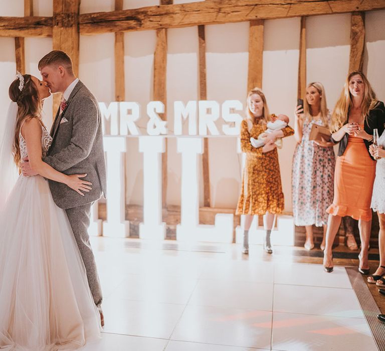 Bride and groom share their first dance on white dance floor in front of light up 'Mr & Mrs Hill' sign