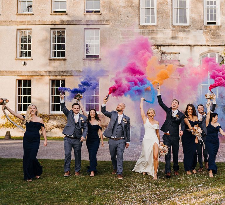 Wedding party outside Elmore Court venue with purple, blue, pink and orange smoke bombs