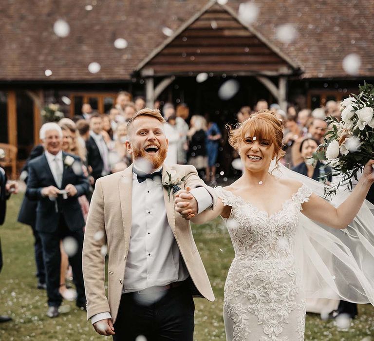 Bride and groom celebrate as they walk through confetti with white and orange wedding bouquet