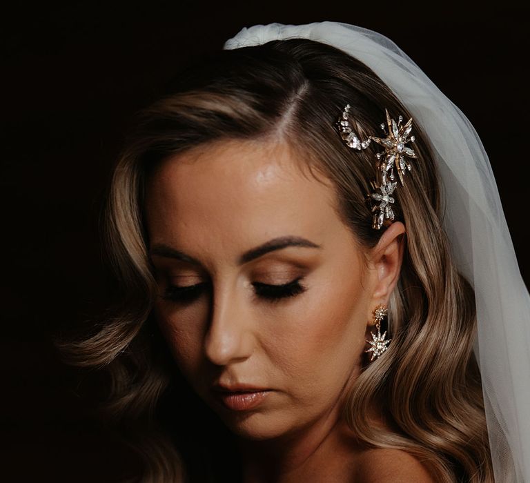 Bride with waved side swept hair has moon and stars gold and silver hair accessory with matching star earrings and veil