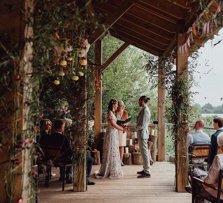 Bride in floral embroiderd wedding dress and groom ingrey suit stand at the altar for their wedding ceremony 