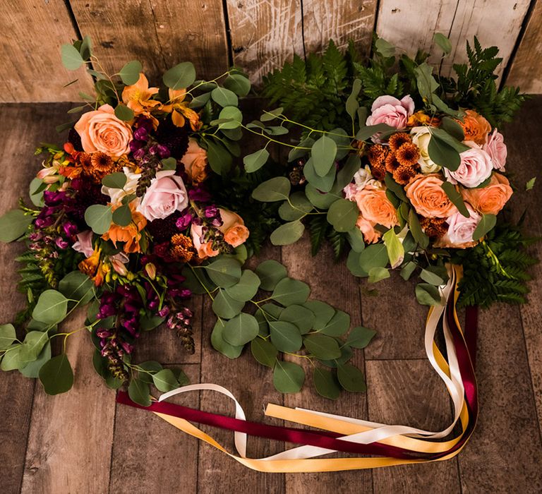 Different wedding bouquets with pink, purple, orange flowers including roses and fern leaves with one tied with multi-coloured ribbons