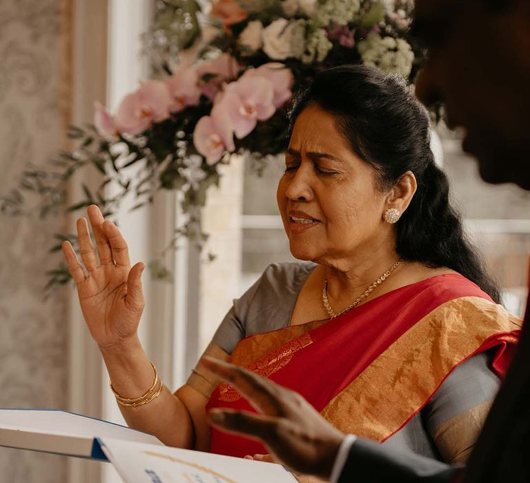 Guest in red and orange garment with golden jewellery, hand raised 