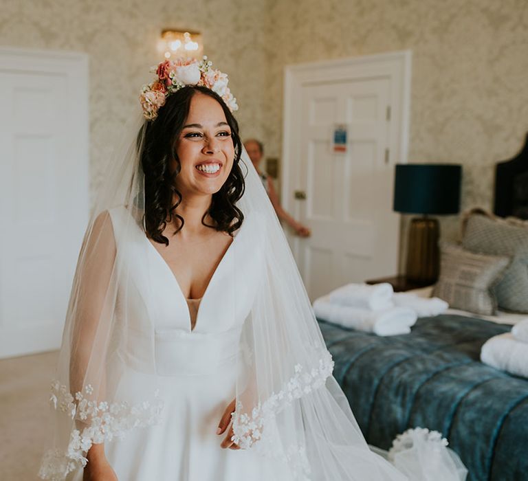 Bride smiles with shoulder length cured hair with pink flower crown and Pronovias flower embroidered veil 