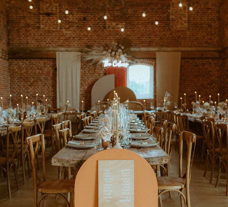 Wooden seating chart sign placed next to table in front of orange arch board with neutral coloured flowers