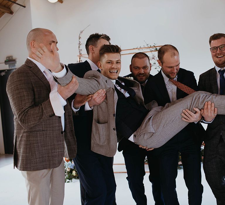 Groom is lifted up by his groomsmen in front of the copper frame and spring flower decor at the altar at Loft Studios 