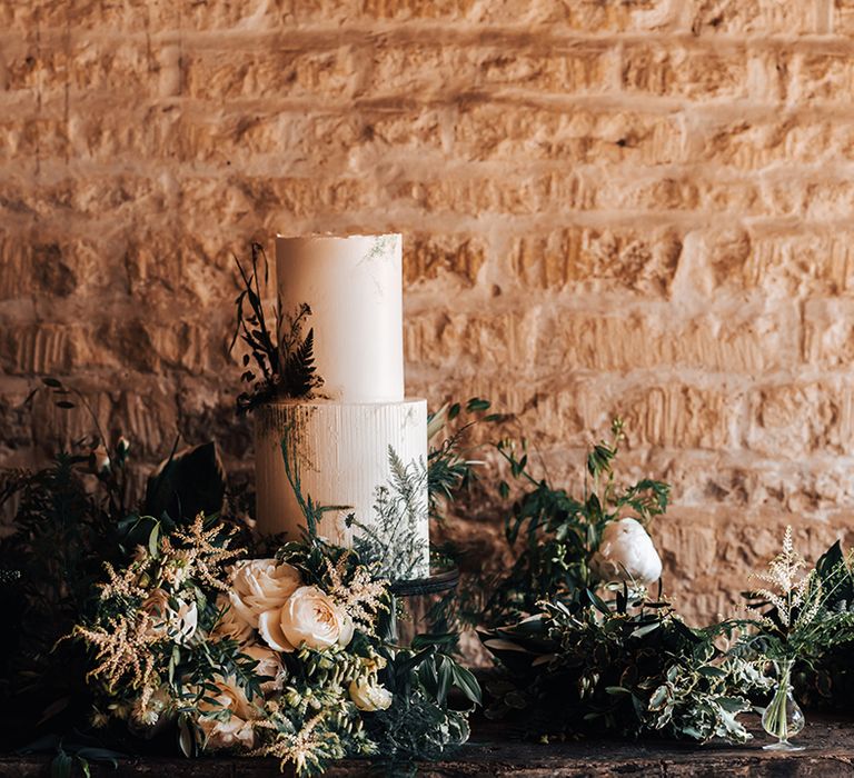 Two tier white buttercream wedding cake surrounded by white and green florals 