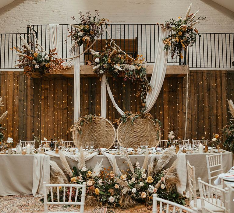 Autumnal orange and warm toned wedding flowers with pampas grass decorate the top table with peacock chairs 