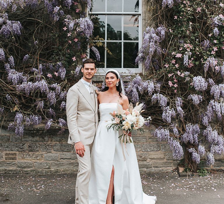 Bride in strapless brocade wedding dress with Manolo Blahnik shoes stands with the groom in a neutral wedding suit