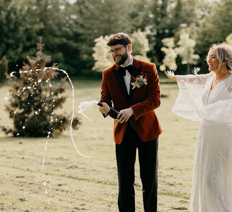 Groom pops a bottle of champagne with bride for their fun retro wedding 