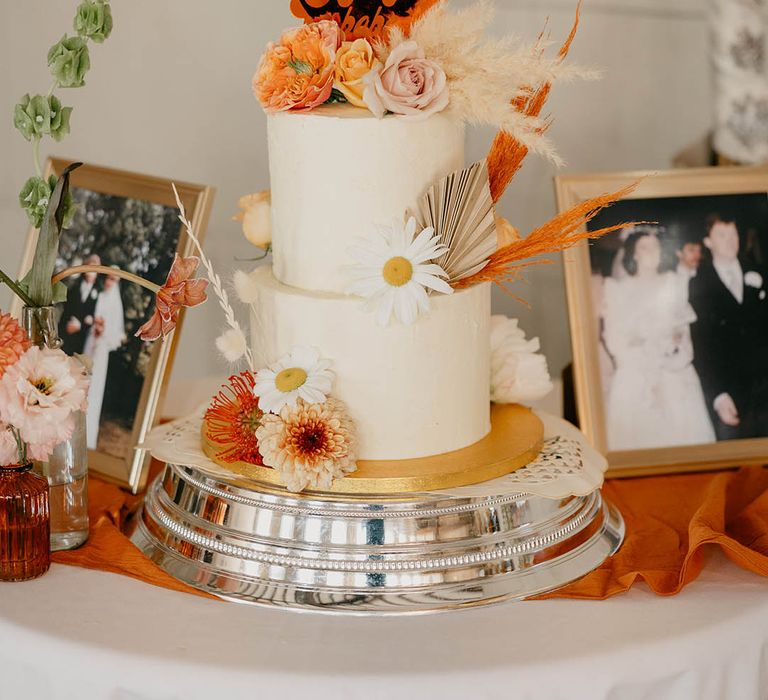 Two tier frosted wedding cake with black and orange heart cake topper reading 'I Got You Babe' for 70s style retro wedding with flower decorations