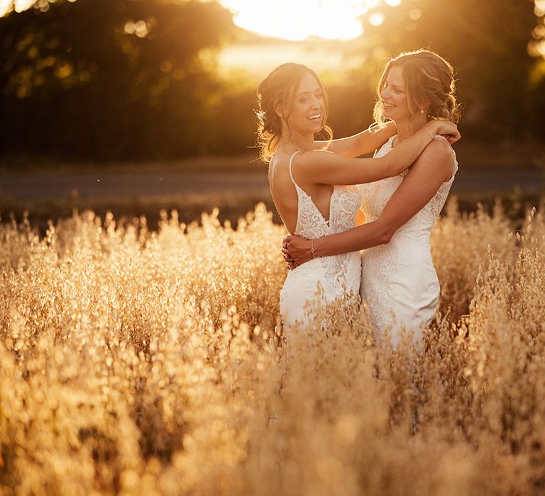 Brides embrace each other as they stand in a field during golden hour 