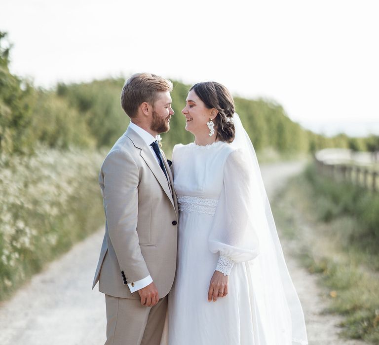 Bride in a vintage wedding dress with a high neck and balloon sleeves with the groom in a cream three piece suit 