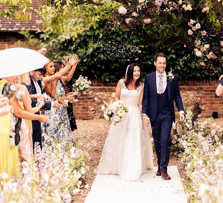 Bride and groom walk back down he aisle as a married couple with white confetti 