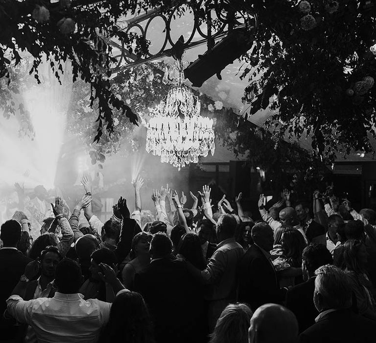 Wedding guests gather for the wedding band playing at the glasshouse marquee reception with chandelier decorations 