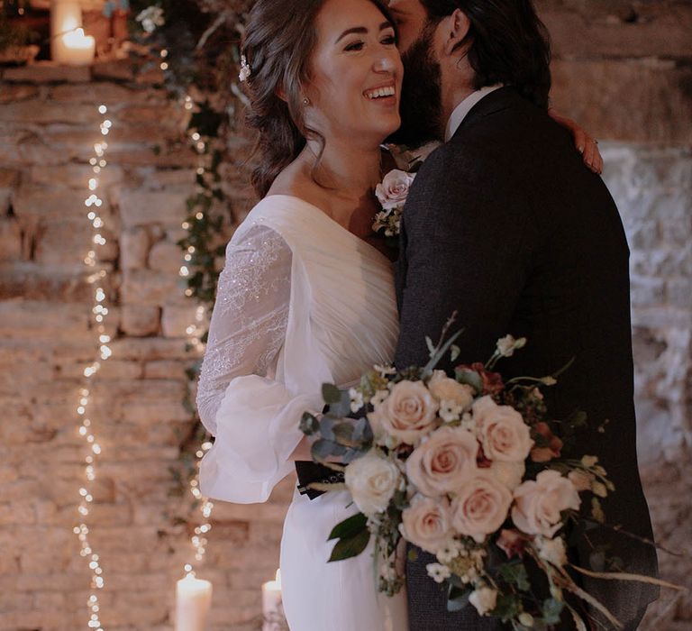 Groom in brown suits kisses the bride on the cheek during their cosy winter wedding ceremony 