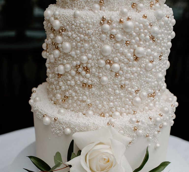 White & gold pearl encrusted wedding cake with white rose floral decor 