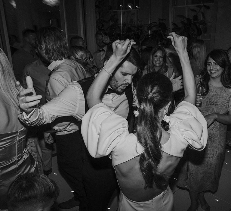 Bride in open back puff sleeve wedding dress and groom in white shirt and waistcoat dancing at wedding party