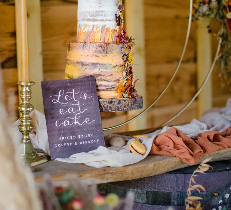 Three tiered vegan buttercream wedding cake in orange, yellow and white with dried florals decorated on the side and handmade calligraphy wedding sign