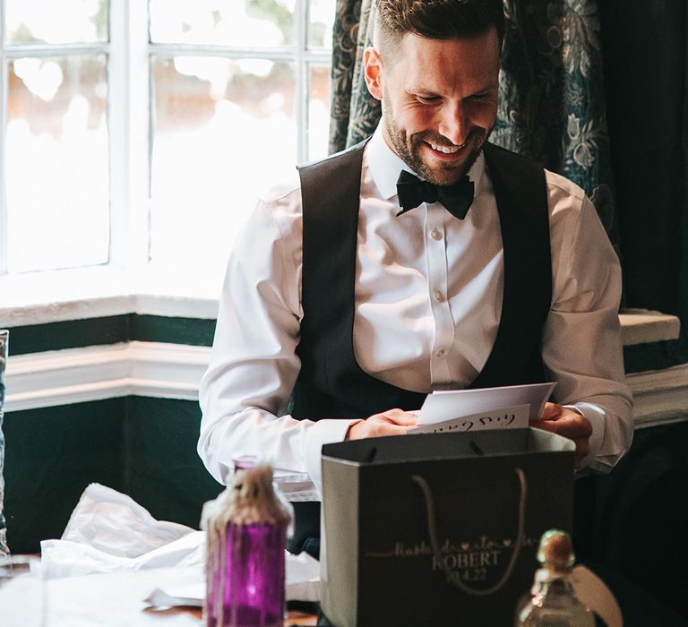 Groom smiles as he opens up a personal letter in black tie on the morning of the wedding 