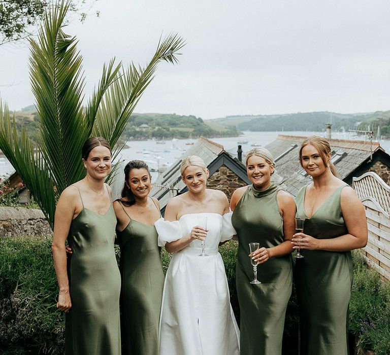 Bride stands with her bridesmaids in different styled satin green bridesmaid dresses 