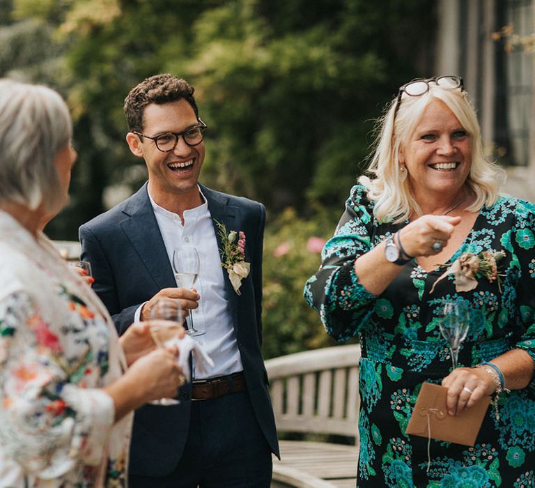 Smiling groom in relaxed navy suit and shirt socialising with the wedding guests for rustic minimal wedding at Askham Hall 